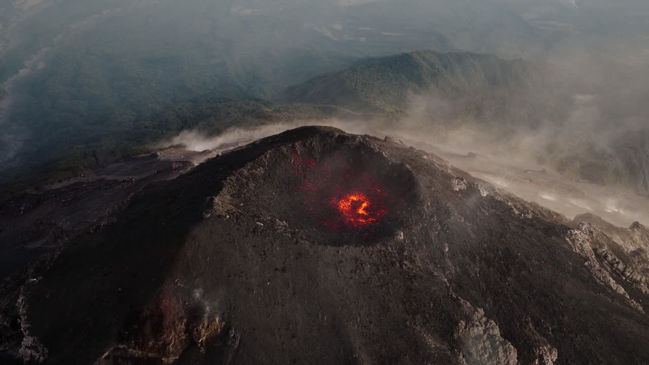 Veduta aerea del cratere del Vulcano Fuego con lava incandescente e vapore che sale sul paesaggio guatemalteco circostante.