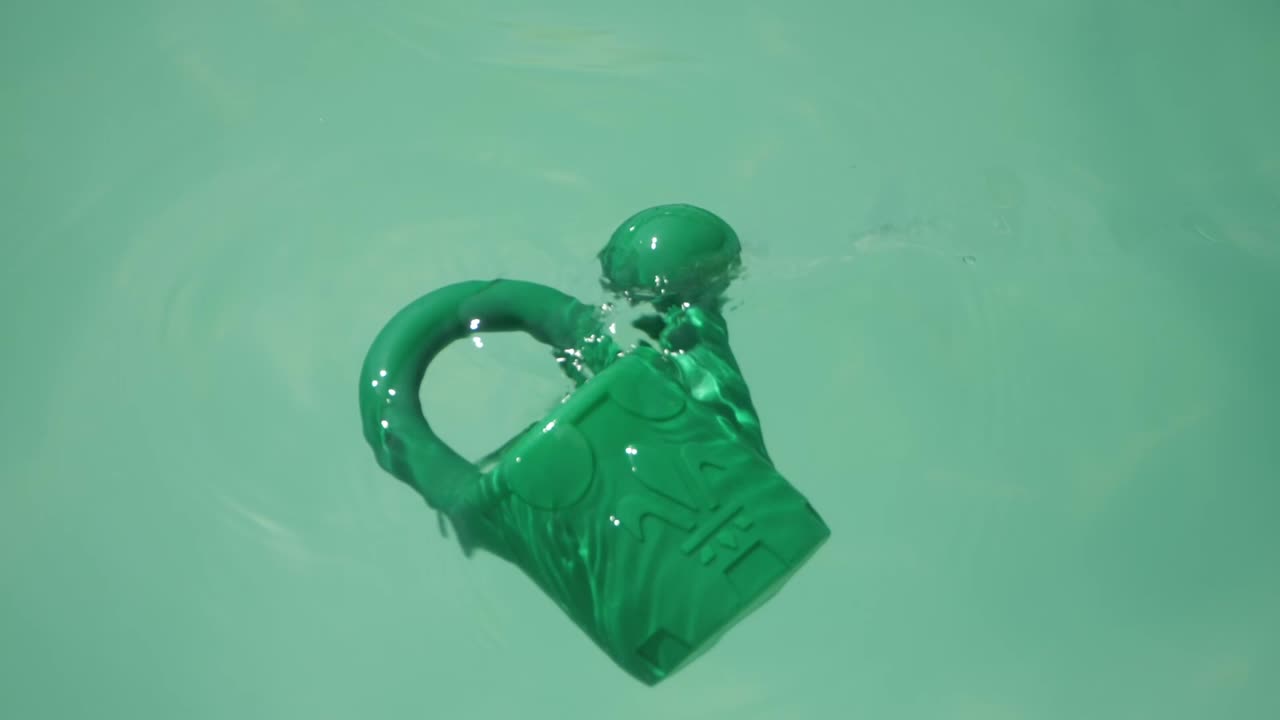 regadera de plástico verde flotando en la superficie de la piscina