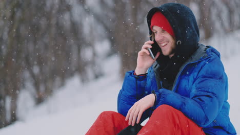 a male snowboarder sitting on the snow takes photos on the phone of a beautiful resort landscape for social networks. resort blogger