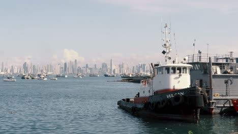 Tug-boat-docked-in-marina-located-at-the-Amador's-Causeway-in-Panama-City,-in-the-distance-a-scenic-backdrop-of-the-spectacular-modern-buildings-and-beautiful-cityscape-of-Panama-City