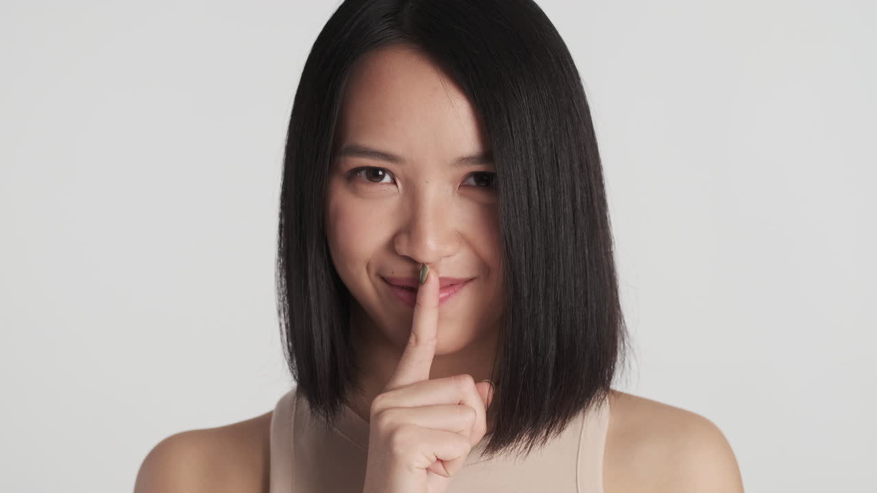 아시아 여성이 카메라 앞에서 침 제스처를 하고 있습니다.