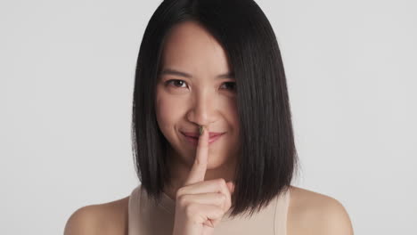 asian woman making silence gesture on camera.