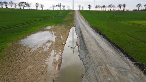 Spiegelung-Der-Windmühle-Im-Wasser,-Windräder-Am-Horizont,-Felder,-Erneuerbare-Energie,-Rotierende-Propeller