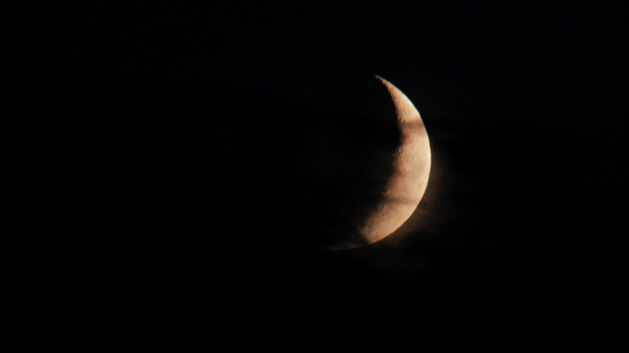 Illuminated crescent moon partially covered by clouds at night