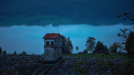 Timelapse,-looking-over-building-rooftop-towards-mountain-backdrop-and-low-level-clouds-below-roof-level