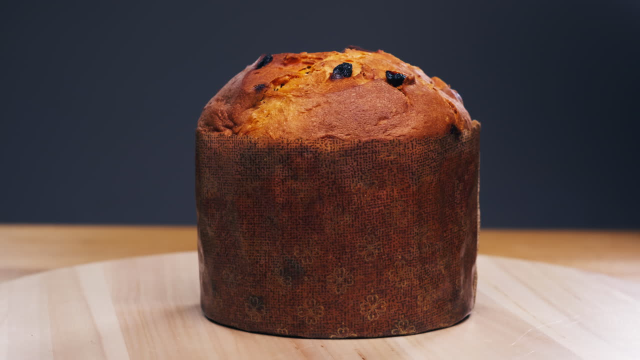 Traditional English Christmas cake tied with a jute thread on the black background. Italian classic Panettone .Pastry Chef sprinkles powdered sugar through a sieve on the fruit Easter cake with raisins. High quality 4k footage