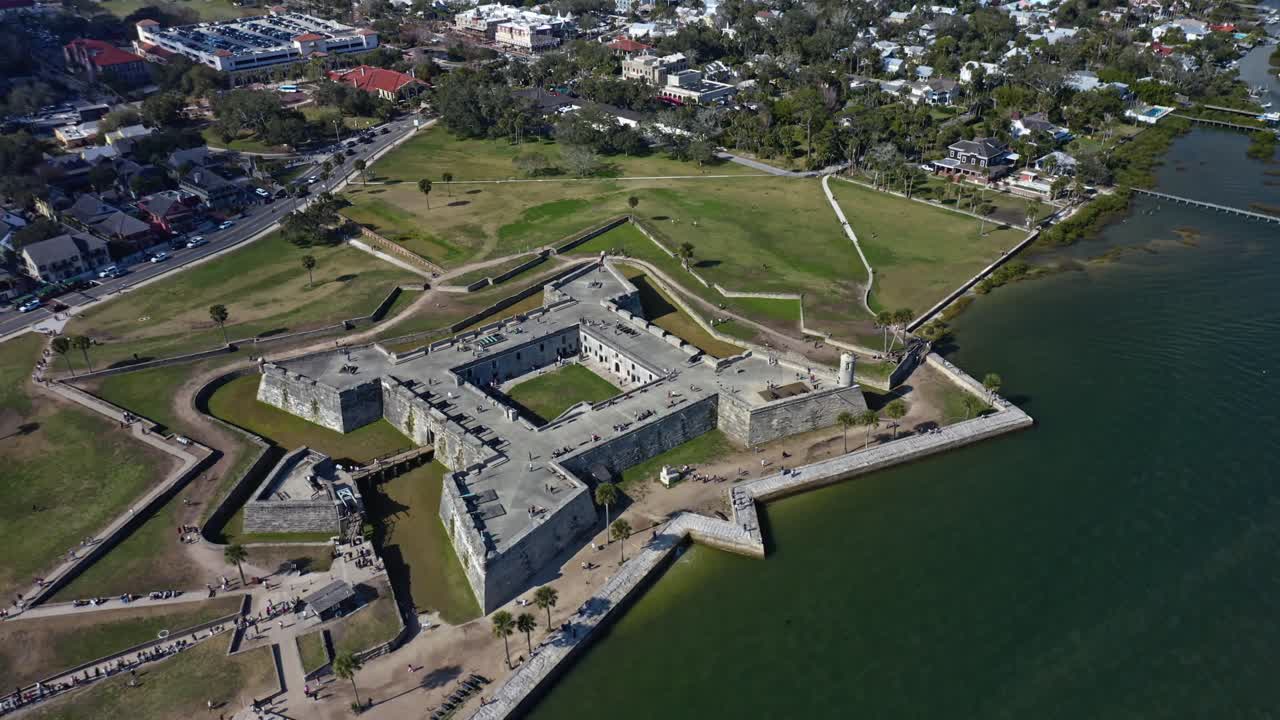 Lo storico Castillo de San Marcos si erge come una grande fortificazione in pietra a St. Augustine, in Florida, circondato da acqua, parchi verdi ed edifici urbani in una giornata parzialmente nuvolosa