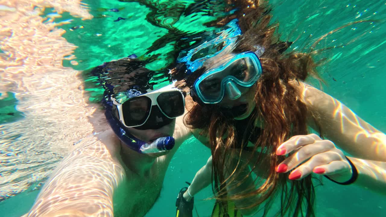 Ungt par tager selfie mens de snorkler i turkisblåt hav, et glædeligt øjeblik