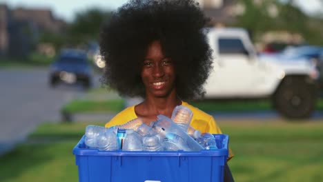 Adolescentes-Afroamericanos-Con-Una-Gran-Sonrisa-Afro-Mientras-Sostiene-Una-Papelera-De-Reciclaje-Llena-De-Botellas-De-Plástico