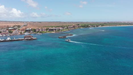 Aerial-wide-tracking-shot-of-a-boat-entering-the-marina-at-Maalaea-Harbor-in-West-Maui,-Hawai'i