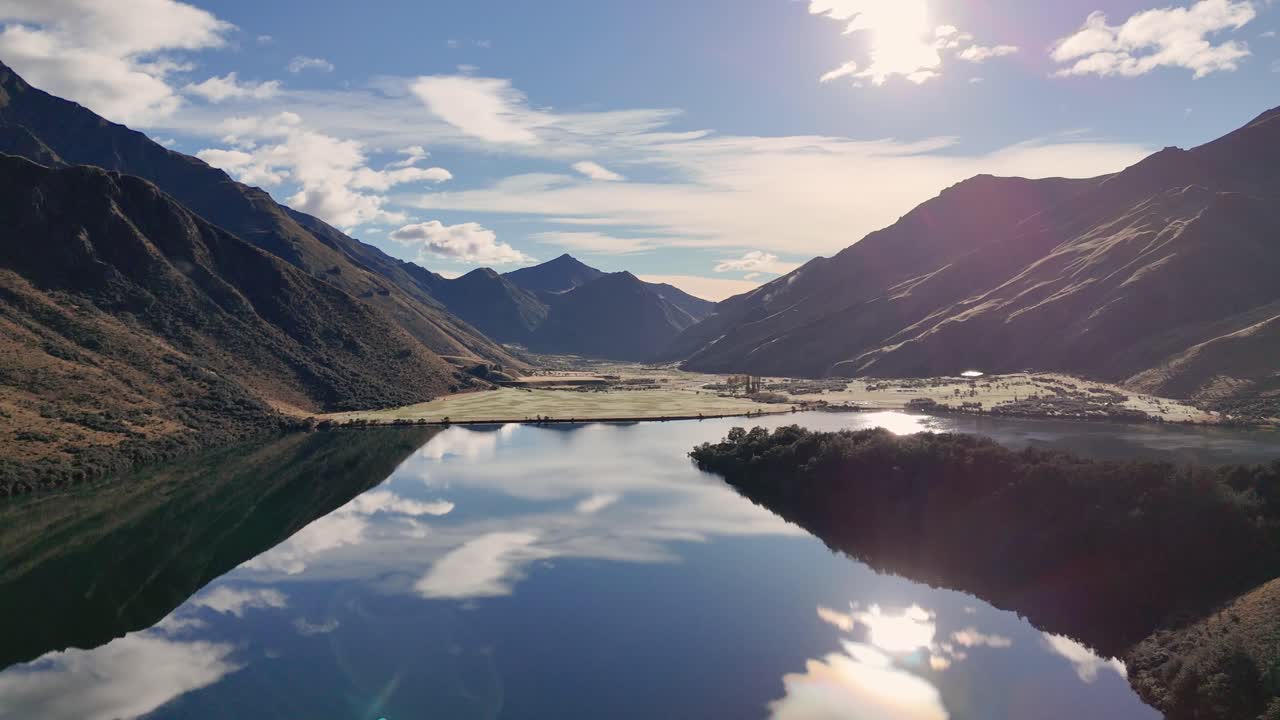 A tranquil lake reflects surrounding mountains under a clear sky, captured in steady daylight with minimal camera movement