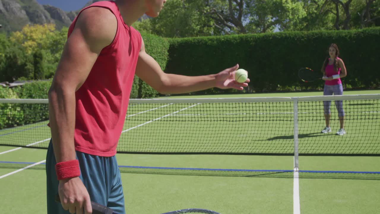 Happy biracial couple playing tennis in garden on sunny day