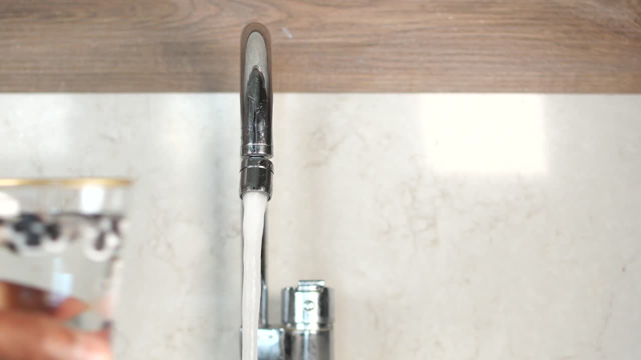 Persona che riempie un bicchiere d'acqua dal rubinetto della cucina