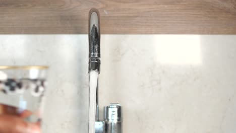 person filling a glass with water from a kitchen faucet
