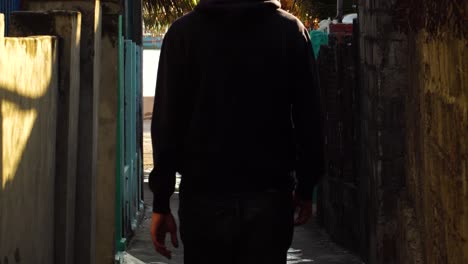 Man-walks-down-narrow-alley-towards-sea-port,-Small-fishing-village-in-Vietnam