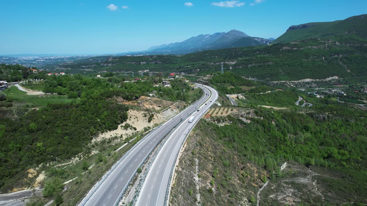 Autostrada di montagna che attraversa colline verdi verso lo skyline in sviluppo della capitale Tirana.
