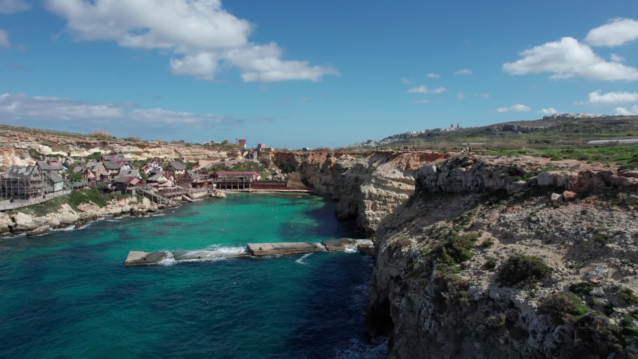 바위가 많은 해안선과 청록색 물이 있는 몰타의 뽀빠이 마을 테마 공원의 조감도