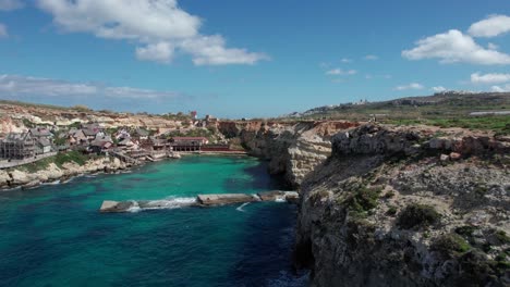 Bird's-Eye-View-Over-Popeye-Village-Theme-Park-In-Malta-With-Rocky-Shoreline-And-Turquoise-Water