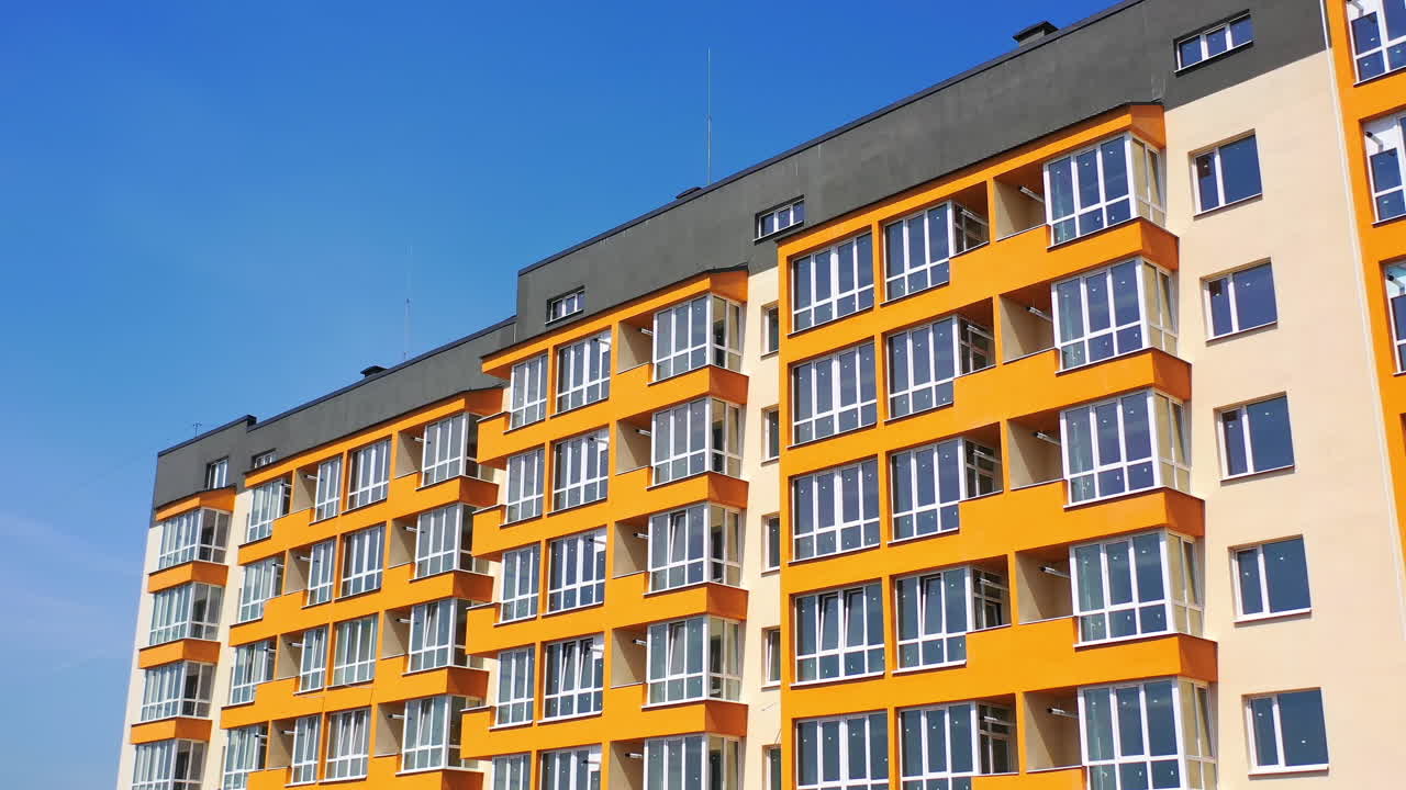 Modern high-rise building against blue sky. Newly built apartment building with colorful walls for urban residents. Bright facade of multi storey city house.