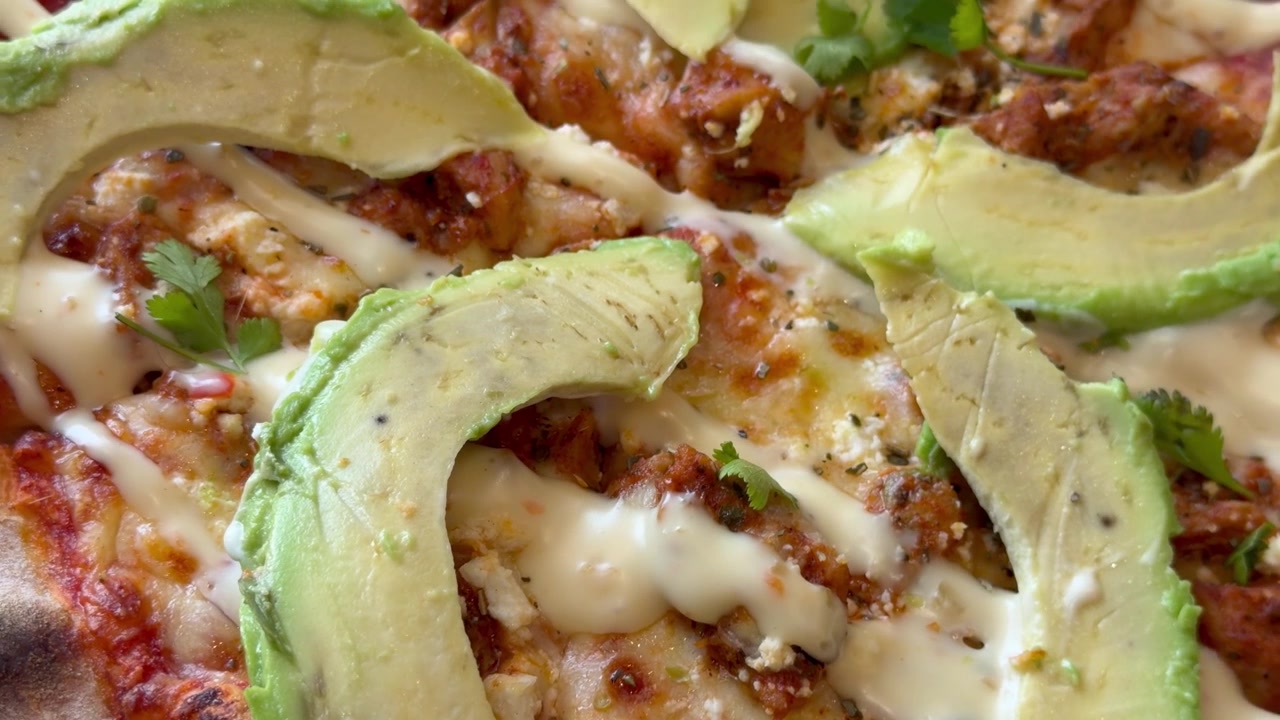 Primo piano di pizza gourmet al pollo con avocado fresco, formaggio fuso e coriandolo