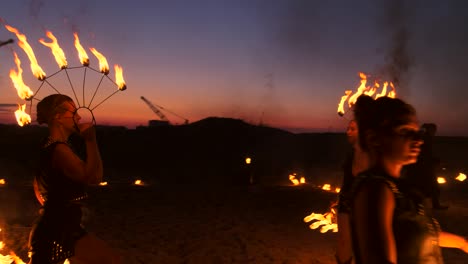 a group of men and woman fire show at night on the sand against the background of fire and tower cranes