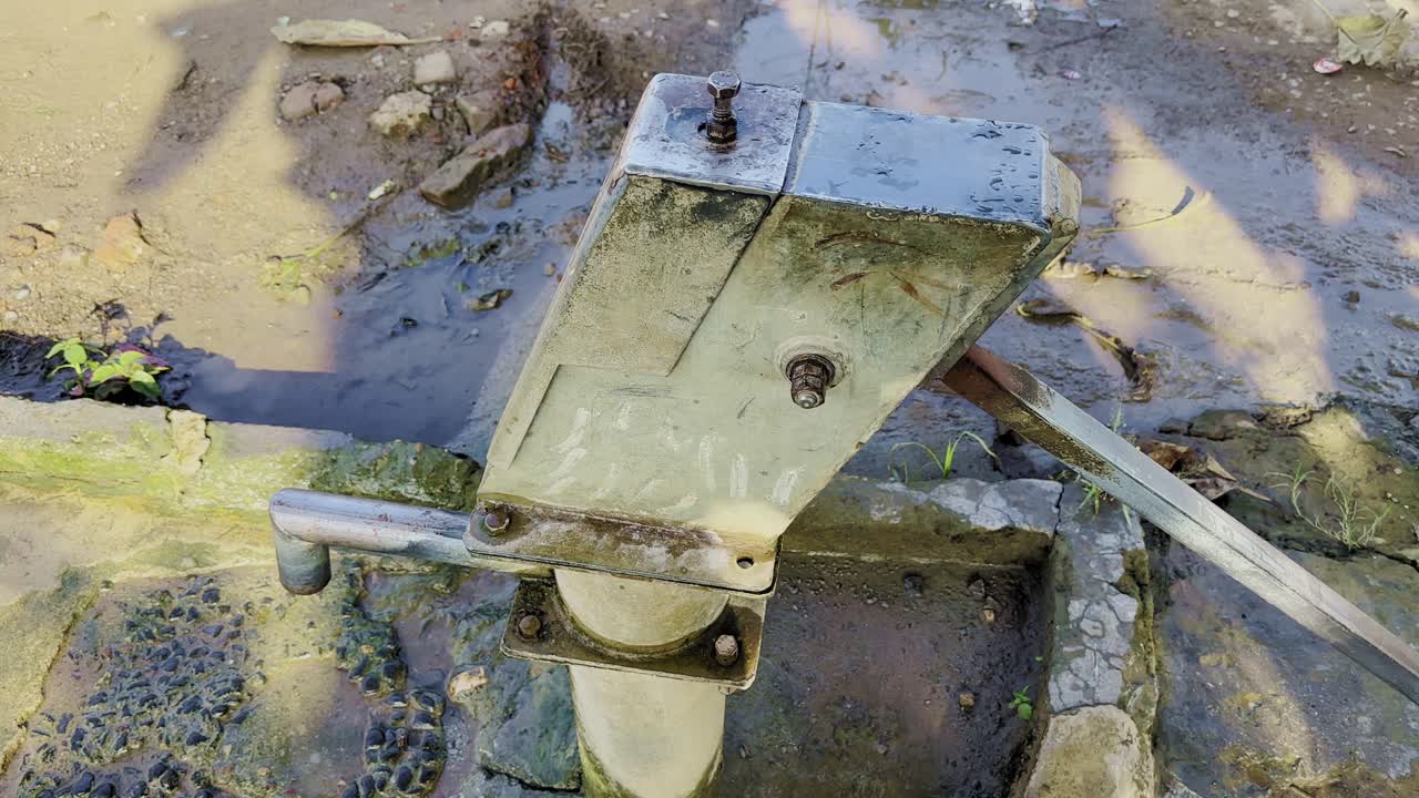 Camera spinning around an old metal hand pump in a muddy rural area, symbolizing traditional water sources, sustainability, and the essence of everyday village life in India