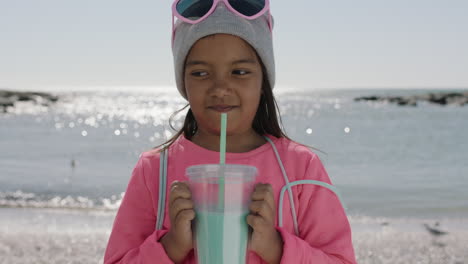 portrait of little girl smiling drinking beverage on beach wearing beanie and pink clothes