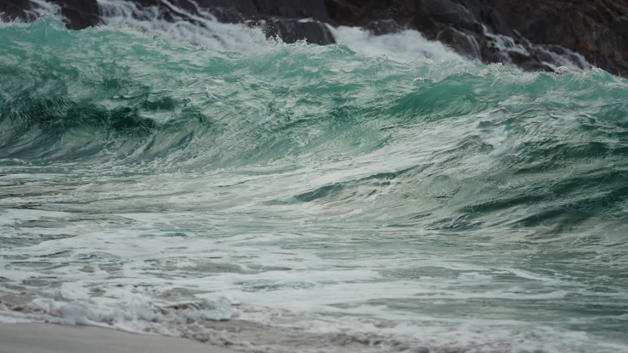 강력한 파도가 바위에 부딪혀 모래사장에 쏟아지고 있습니다.