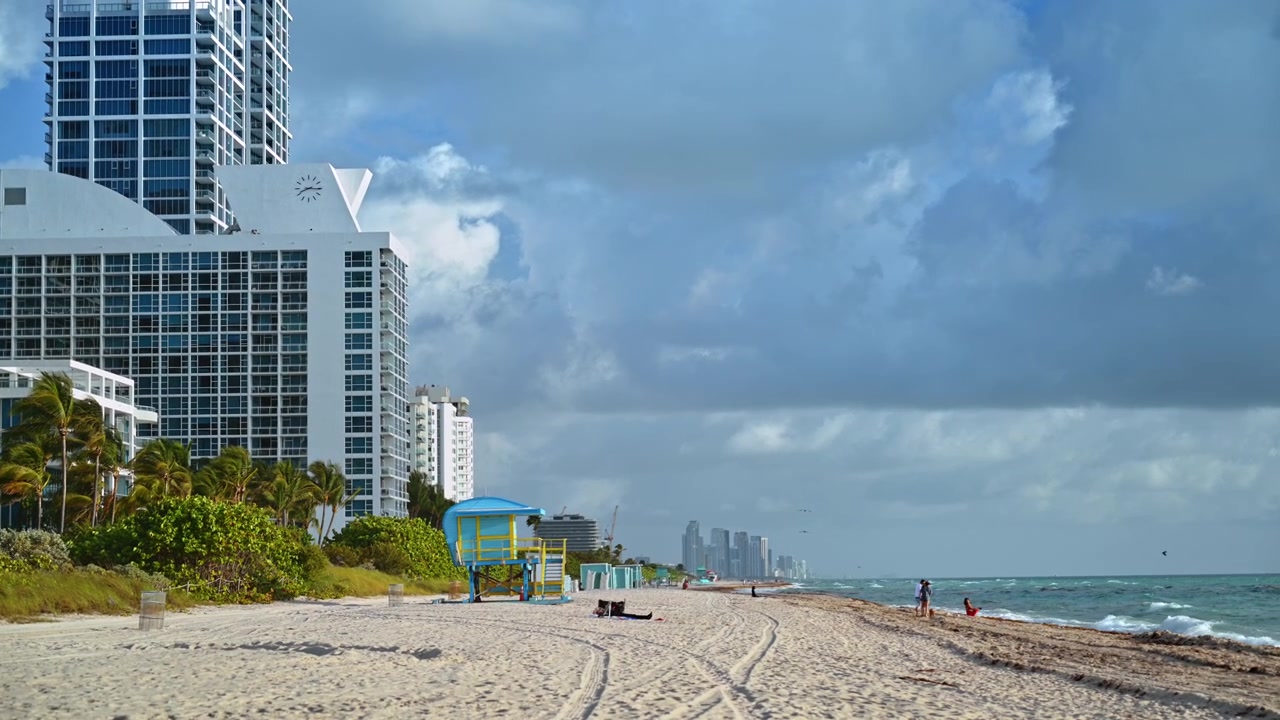 Litorale di Miami Beach con condomini e nuvole temporalesche. Condomini fronte mare, torretta blu del bagnino, tracce sulla sabbia, oceano, persone e nuvole temporalesche a Miami Beach.