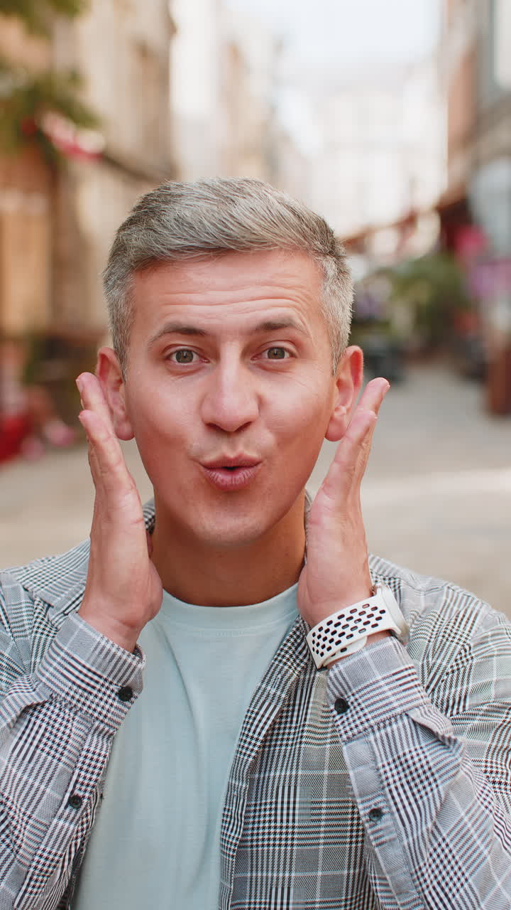 hombre maduro mirando sorprendido a la cámara con los ojos abiertos conmocionado por la victoria repentina en la calle