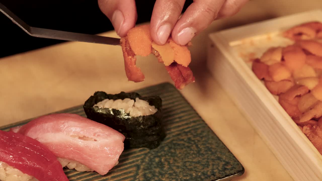 Nahaufnahme eines Sushi-Kochs, der mit ruhiger Kameraaufnahme von oben sorgfältig Seeigel-Gunkan formt