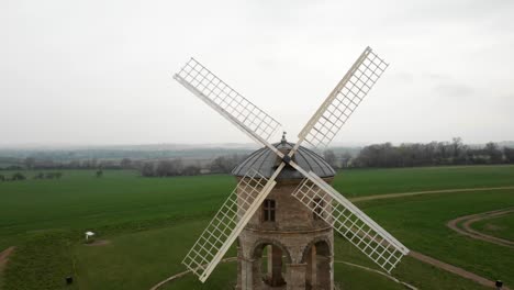Drone fly-through shot between the sails of a historic windmill surrounded by fields.