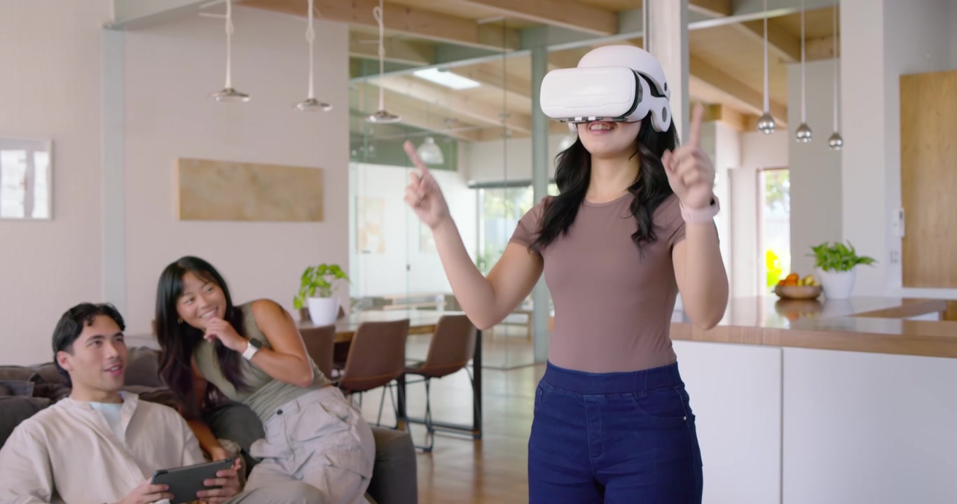 Donna in piedi con visore VR che risponde ai comandi, mostrando una demo agli amici con un tablet sul divano.