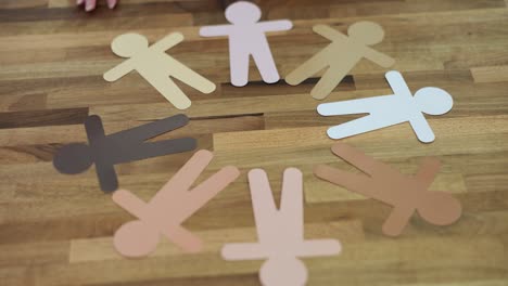 diverse paper cut-out people arranged in a circle on a wooden table