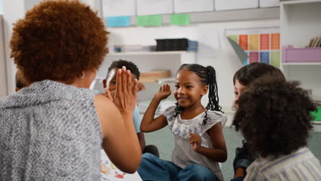 Female-Teacher-Reads-And-Gives-High-Fives-To-Multi-Cultural-Elementary-School-Pupils-In-Class