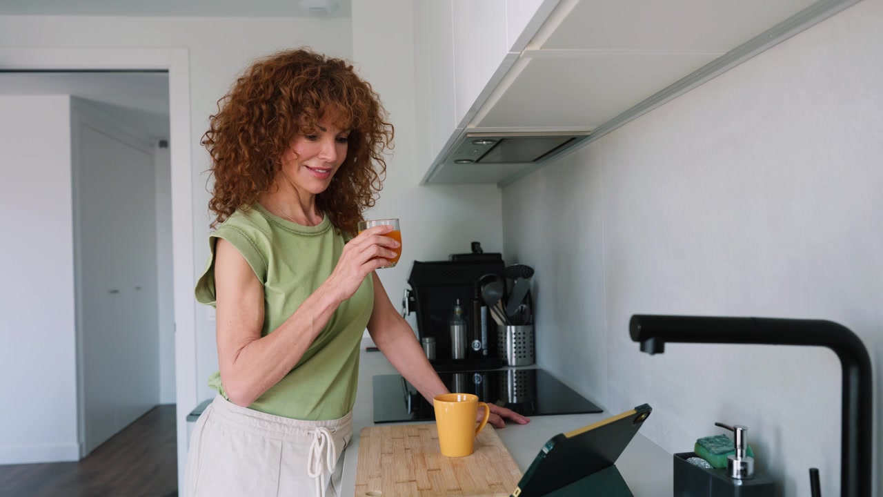 Donna che beve succo fresco mentre usa un tablet in una cucina moderna
