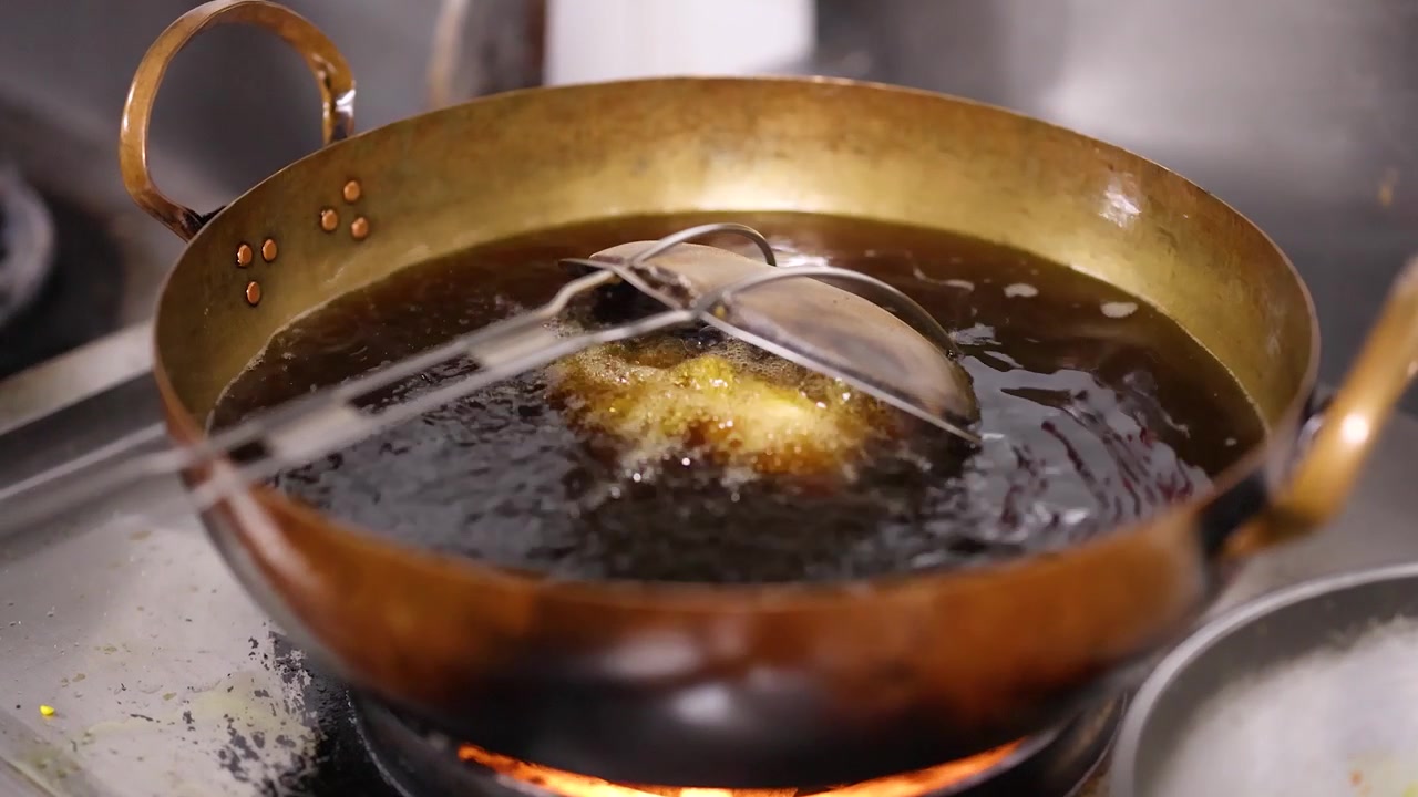 Close-up shot of savory pastries deep frying in hot oil within a traditional brass wok.