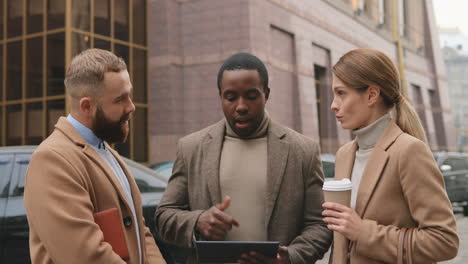 bottom view of caucasian businesswoman holding coffee, african american man watching to a tablet and caucasian man talking in the street in autumn