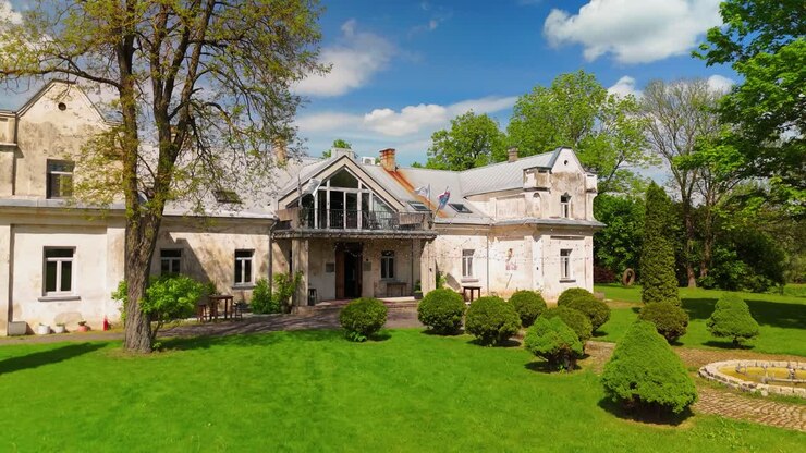 Vue aérienne du Manoir de Babtyno, un domaine historique entouré d'une végétation luxuriante, présentant une architecture classique et un jardin bien entretenu. Thèmes liés à l'histoire, au patrimoine et aux domaines ruraux.