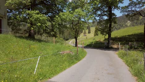 Biking-on-a-single-lane-road-through-a-rural-mountain-village-near-Pragel-Pass,-Switzerland