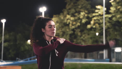 sportive curly girl stretching and rotating arms in the park at night 1