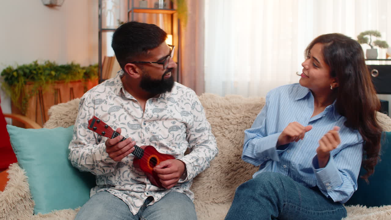 Indian family couple man woman laughing dancing at home playing toy ukulele in joyful fun moment