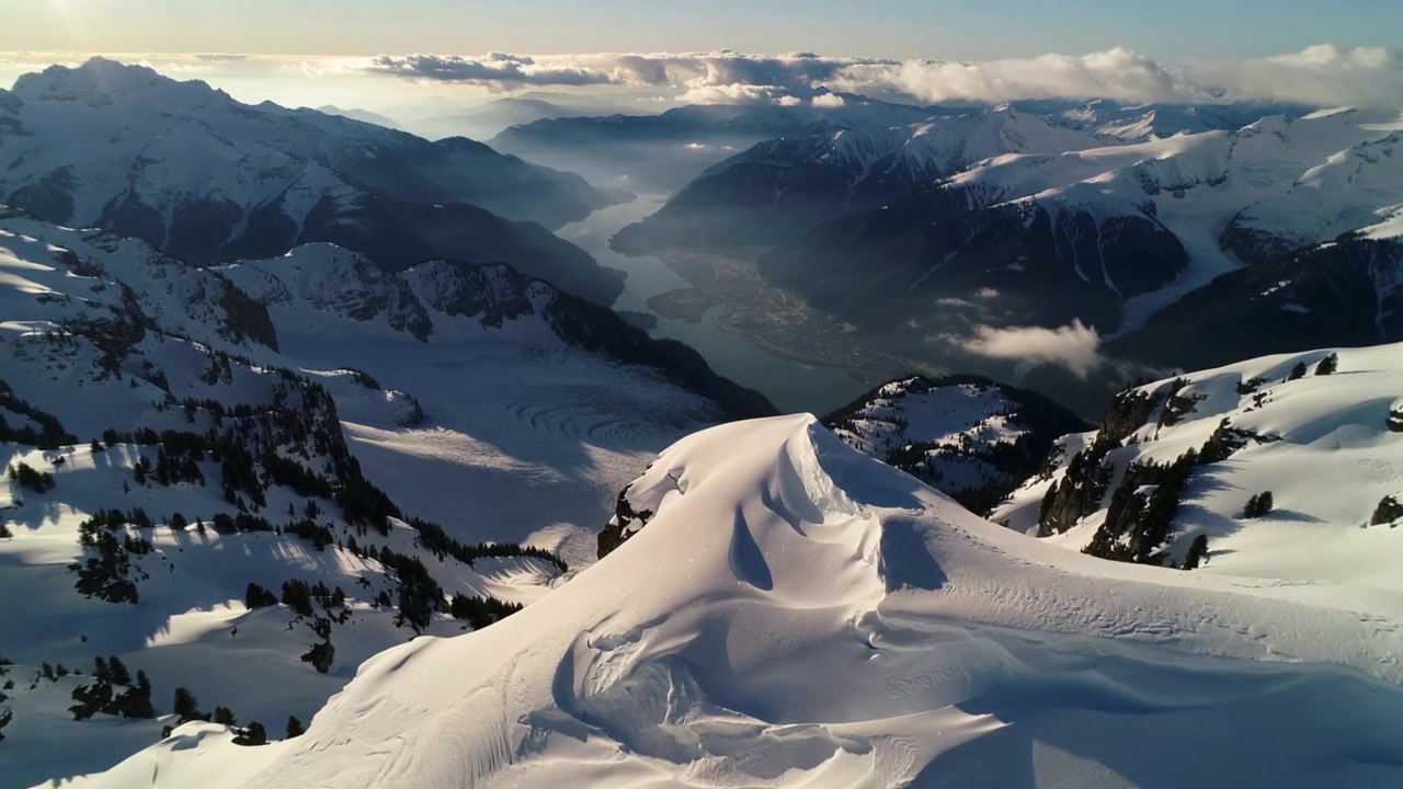 Drone moving forward and descending over alpine ridge at sunrise, revealing wind-sculpted cornice