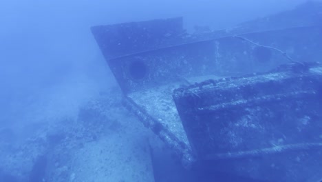Cinematic close-up dolly shot through a submarine porthole of the eerie hull of a shipwreck at the bottom of the ocean off the coast of Hawai&#039;i