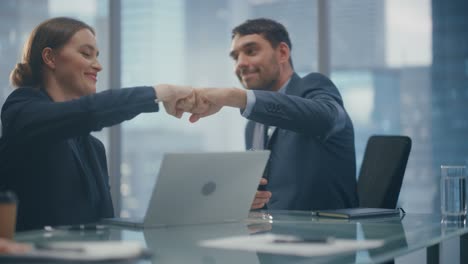 corporate ceo and investment manager talking, using laptop computer while sitting in meeting room in office. two happy smiling businesspeople fist bump over a lucrative e-commerce investment deal.