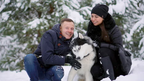 family portrait of cute happy couple hugging with their alaskan malamute dog licking man's face. funny puppy wearing santa christmas deer antlers and kissing woman. freedom lifestyle pet lovers.