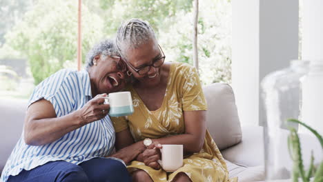 Glückliche-ältere-Afroamerikanische-Freundinnen,-Die-Kaffee-Trinken-Und-Im-Wohnzimmer-Lachen,-Zeitlupe