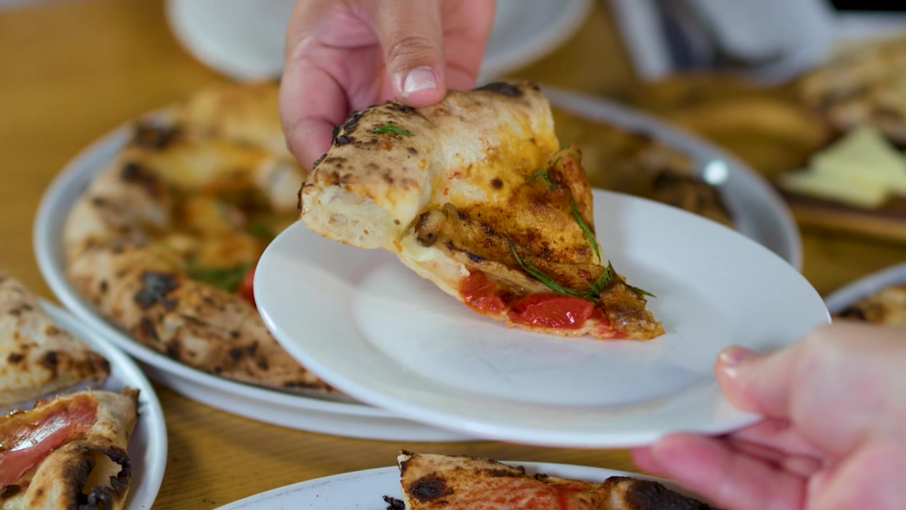Primo piano di una mano che serve una fetta di pizza gourmet su un piatto di ceramica bianco