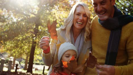 mom dad and daughter holding leaves and smiling outdoors