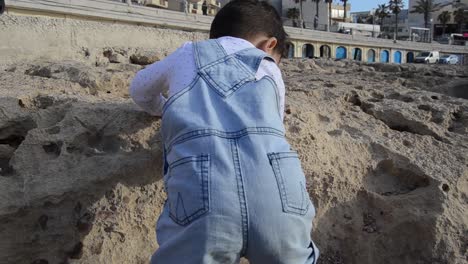 Cute-child,-two-years-old-boy-going-down-stone-in-front-of-boat-houses-in-Buggiba-Malta